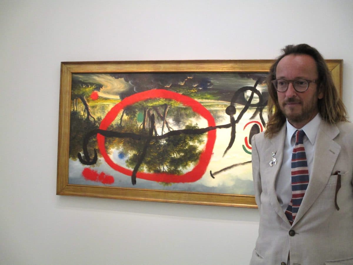 Le petit-fils de Joan Miró, Joan Punyet Mirό, devant l’œuvre (teintée de malice…) : Personnage au lever du soleil au bord d’une rivière – 10 juillet 1965 – Huile sur toile de style pompier –
Successió Miró – © DR